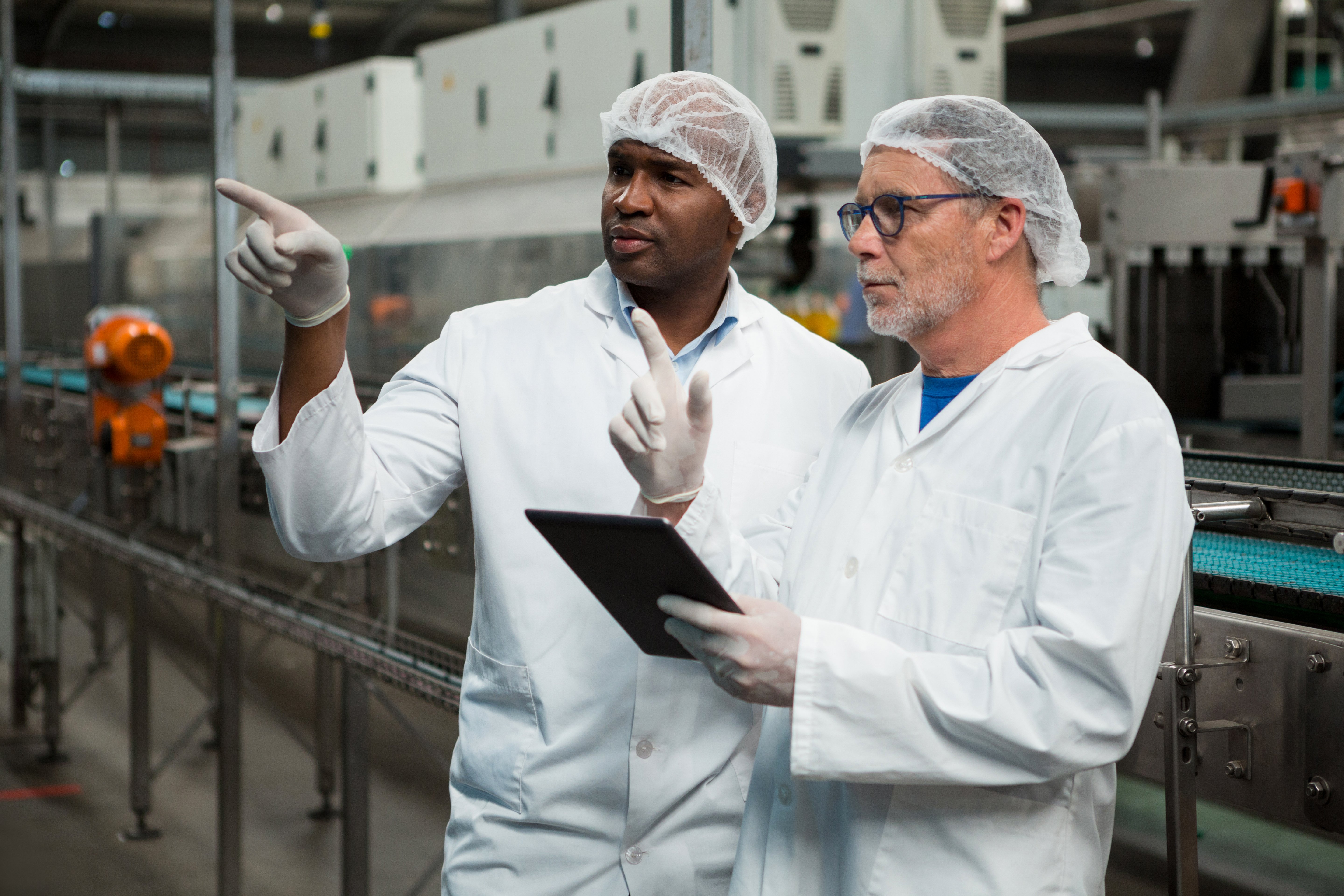 Food manufacturing workers wearing protective gear inspecting products on a production line, representing staffing and food safety quality assurance challenges